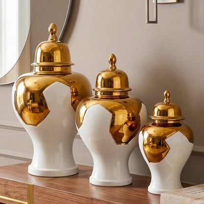Ornate white and gold decorative vase  displayed on a wooden surface against a deep green wall, with its lid placed beside it.