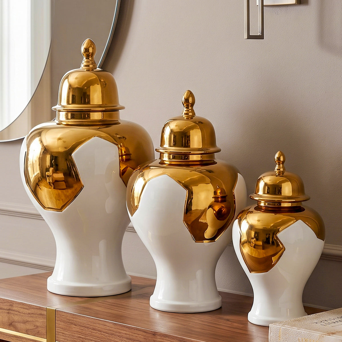 Three decorative ceramic canisters with shiny gold lids and white bodies, arranged on a wooden console table in an interior setting.