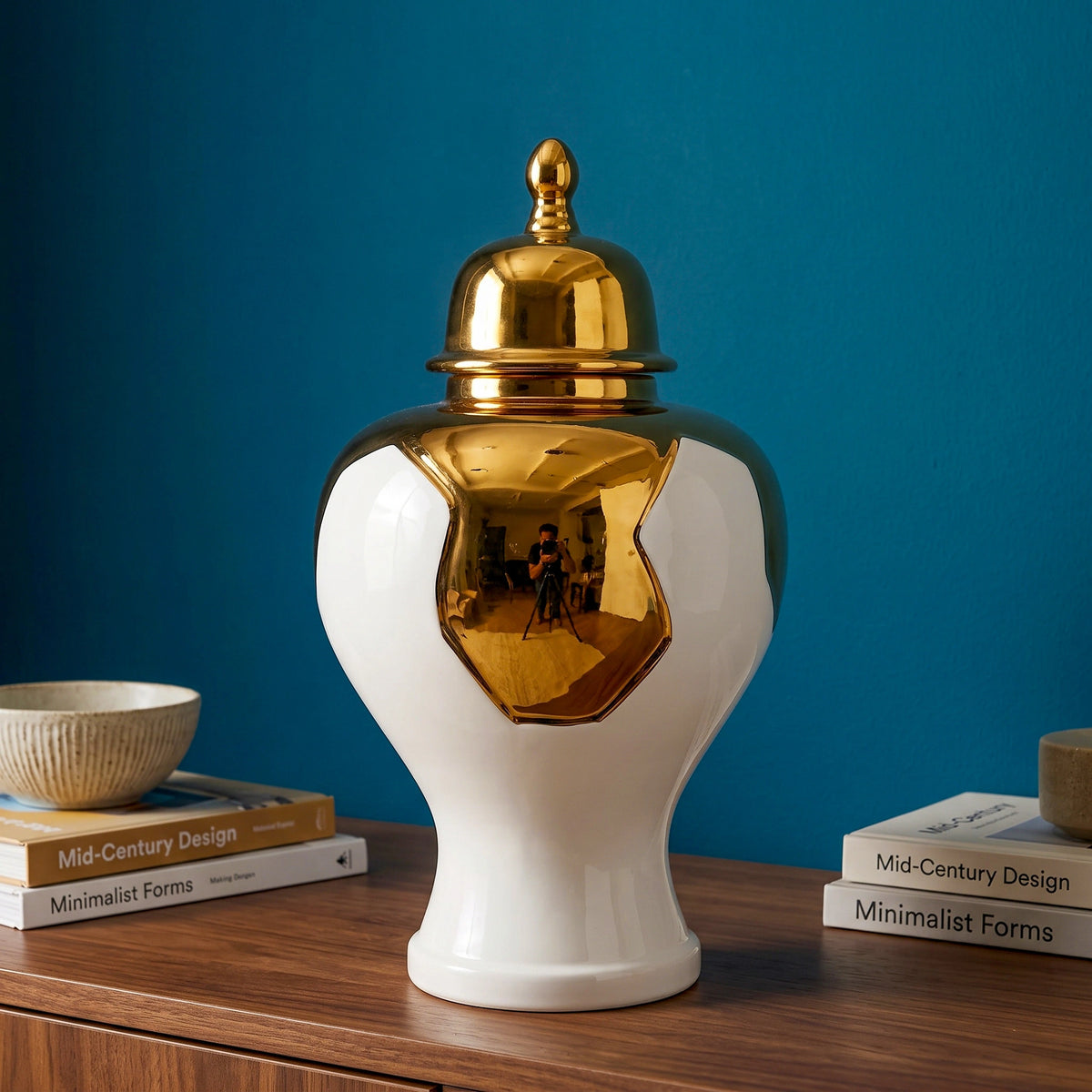 Ornate white and gold decorative vase  displayed on a wooden surface against a blue wall, with its lid placed beside it.