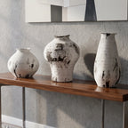 A modern console table with a dark wood top and metal legs, styled in a living room setting with three white and black textured ceramic vases on top and a stack of books underneath.