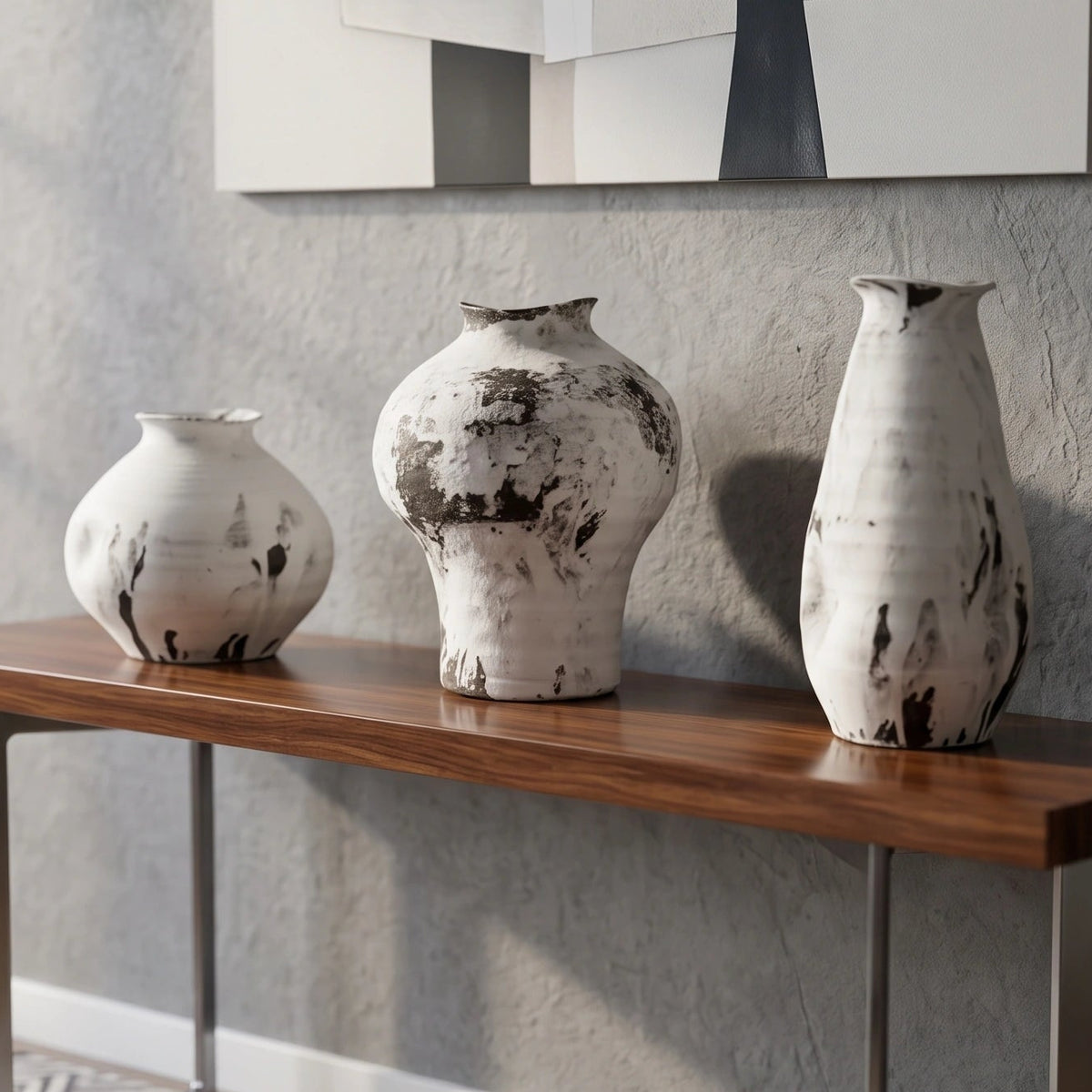 A modern console table with a dark wood top and metal legs, styled in a living room setting with three white and black textured ceramic vases on top and a stack of books underneath.