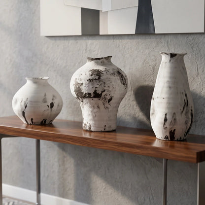 A modern console table with a dark wood top and metal legs, styled in a living room setting with three white and black textured ceramic vases on top and a stack of books underneath.