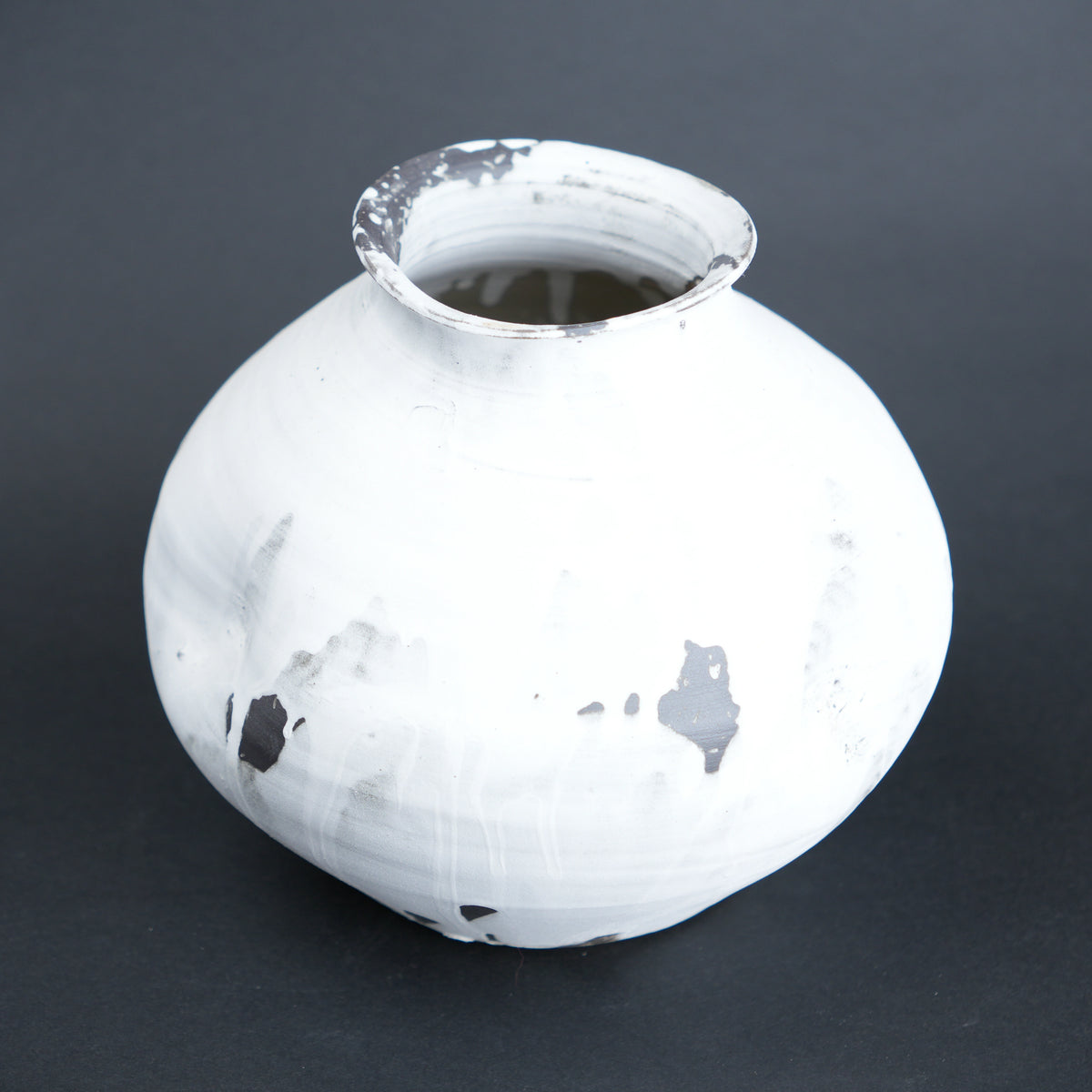 White ceramic vase with black speckles on a dark gray background