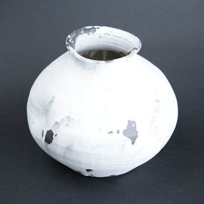 White ceramic vase with black speckles on a dark gray background