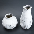 Two white ceramic vases with black speckles on a dark gray background