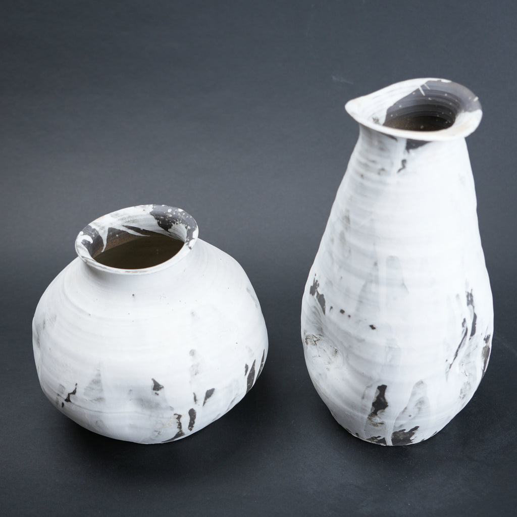 Two white ceramic vases with black speckles on a dark gray background