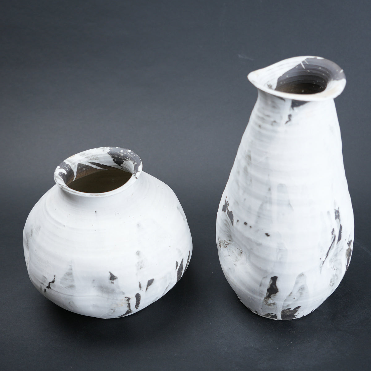 Two white ceramic vases with black speckles on a dark gray background