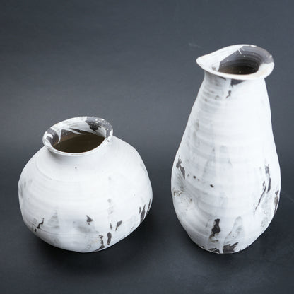 Two white ceramic vases with black speckles on a dark gray background