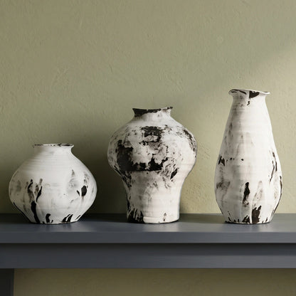 Three hand-painted ceramic vases with a distressed black and white textured glaze, displayed on a dark gray console table against a textured sage green wall.
