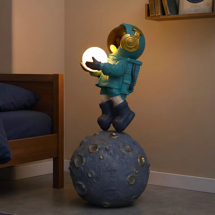 Teal astronaut figurine with gold visor holding a glowing orb while standing on a large crater-textured moon base.