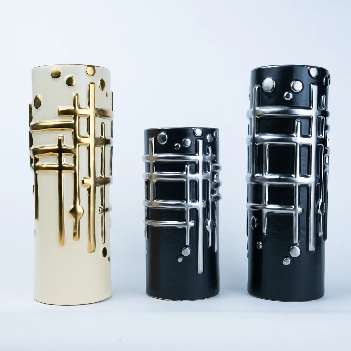 Three cylindrical decorative vases with a modern geometric design, shown in cream, black, and glossy black sizes against a light gray background.