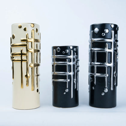 Three cylindrical decorative vases with a modern geometric design, shown in cream, black, and glossy black sizes against a light gray background.
