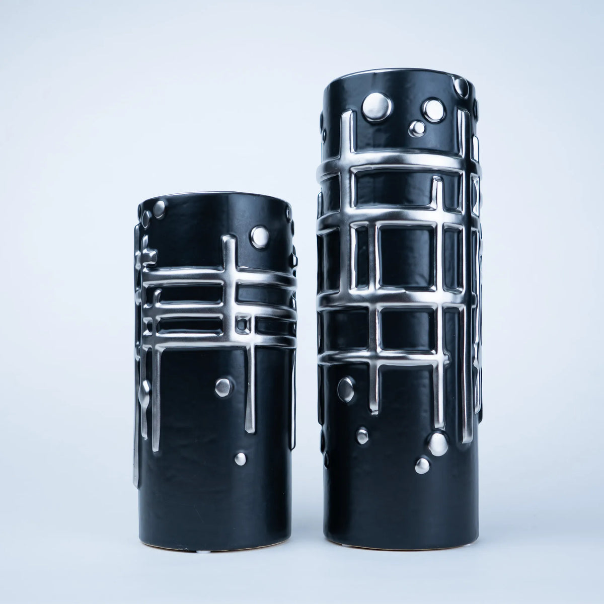 Two black ceramic vases with a glossy finish and raised silver geometric patterns, displayed on a light gray background.