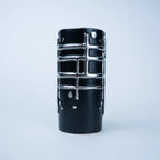 A black ceramic vase with a textured, ribbed body and raised silver metallic grid patterns, photographed against a clean, light gray studio background.