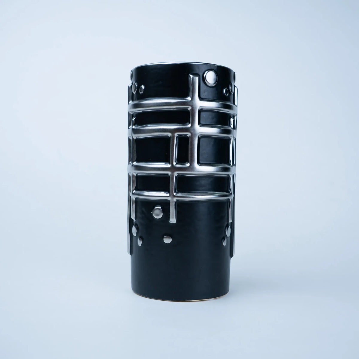 A black ceramic vase with a textured, ribbed body and raised silver metallic grid patterns, photographed against a clean, light gray studio background.