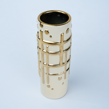 A modern cylindrical ceramic vase in cream with a gold grid pattern and perforated details, set against a light blue background.