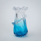 Glass vase with blue base and ruffled top on a light gray background