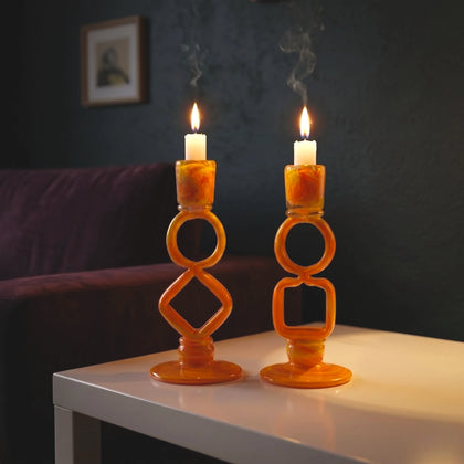 Two orange candle holders with lit candles on a table against a dark wall.