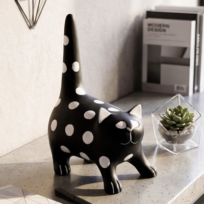 A black cat-shaped desk lamp or figurine with white polka dots, standing on a gray tabletop next to a small succulent in a glass terrarium.