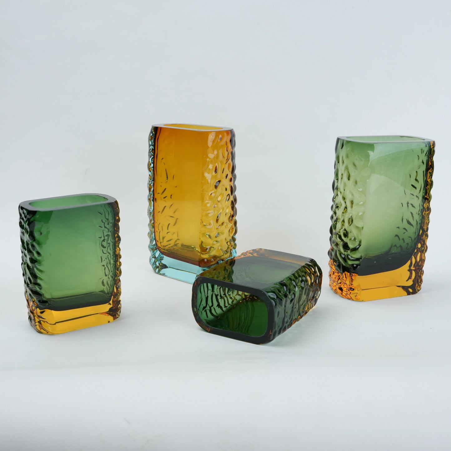 Set of four textured glass vases in green and amber on a light gray background