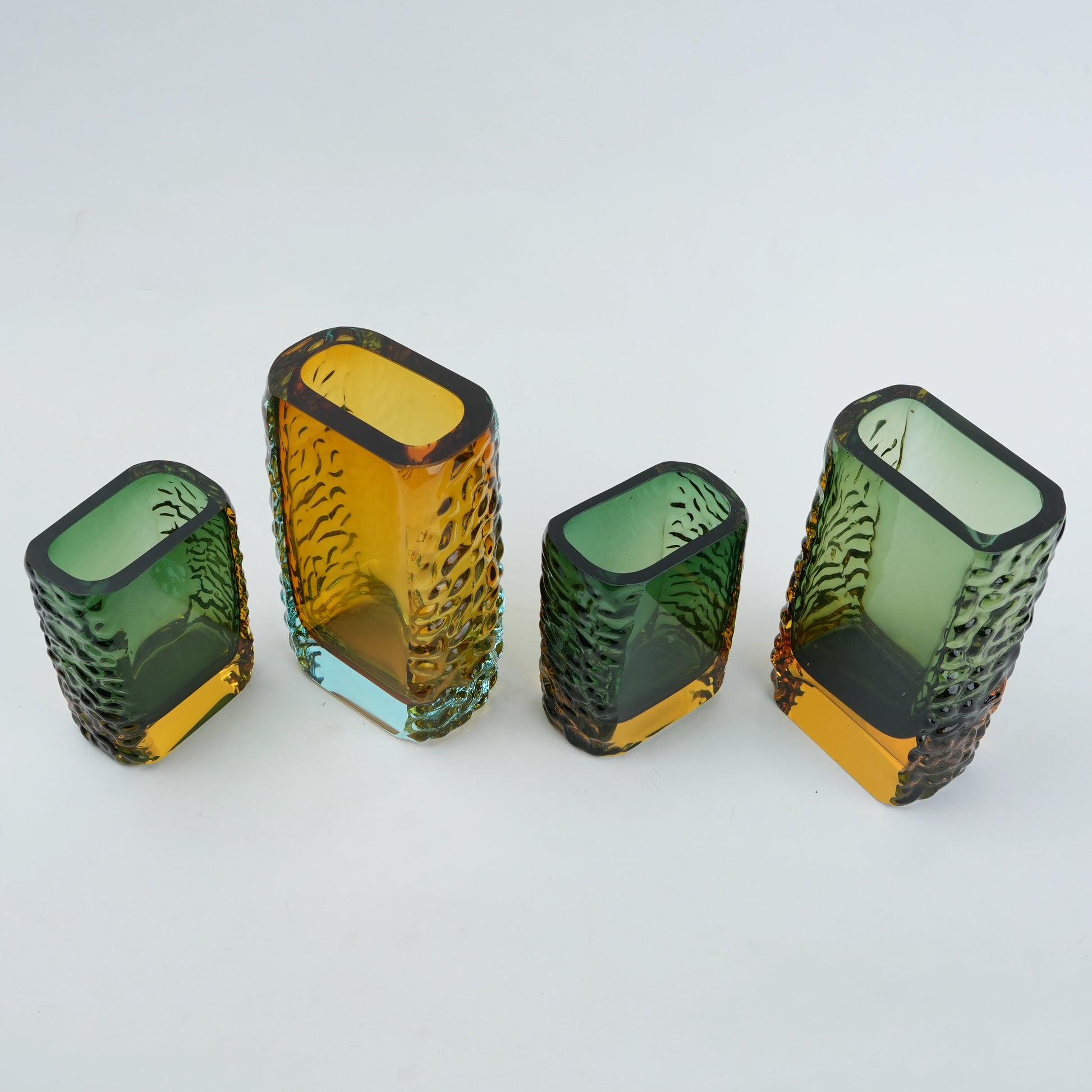 Four textured glass vases in green and yellow on a white background