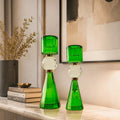 Two green faceted glass candlestick holders with clear crystal spheres and gold-tone accents, displayed on a marble console table in a modern interior setting.
