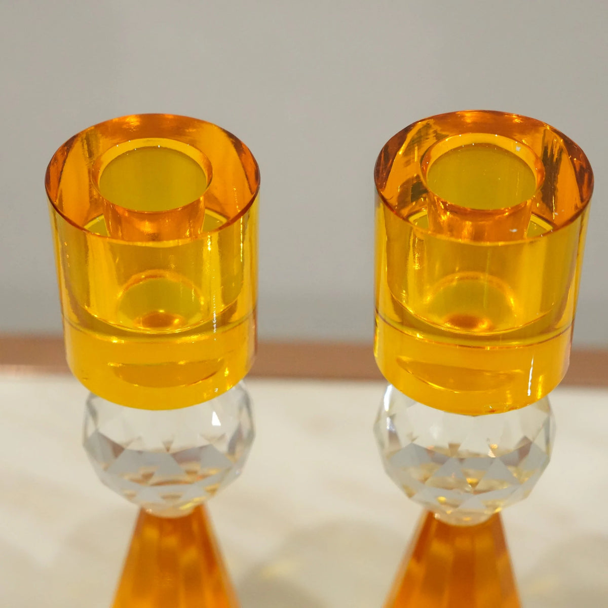 Two orange candle holders on a reflective surface with a neutral background
