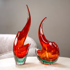 Two red and green glass sculptures on a white surface with a neutral background