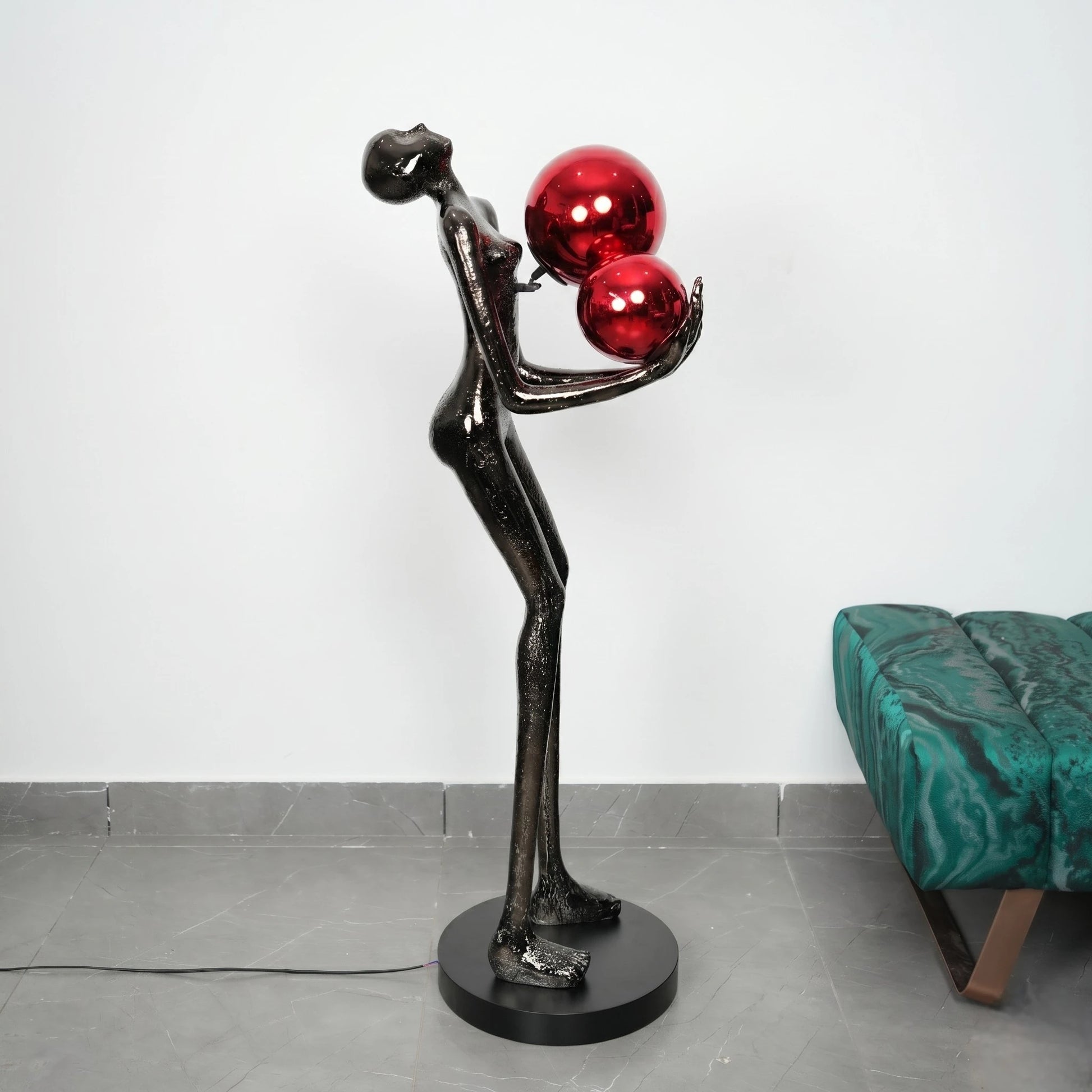 Statue of a figure holding red spheres on a gray floor with a green chair in the background