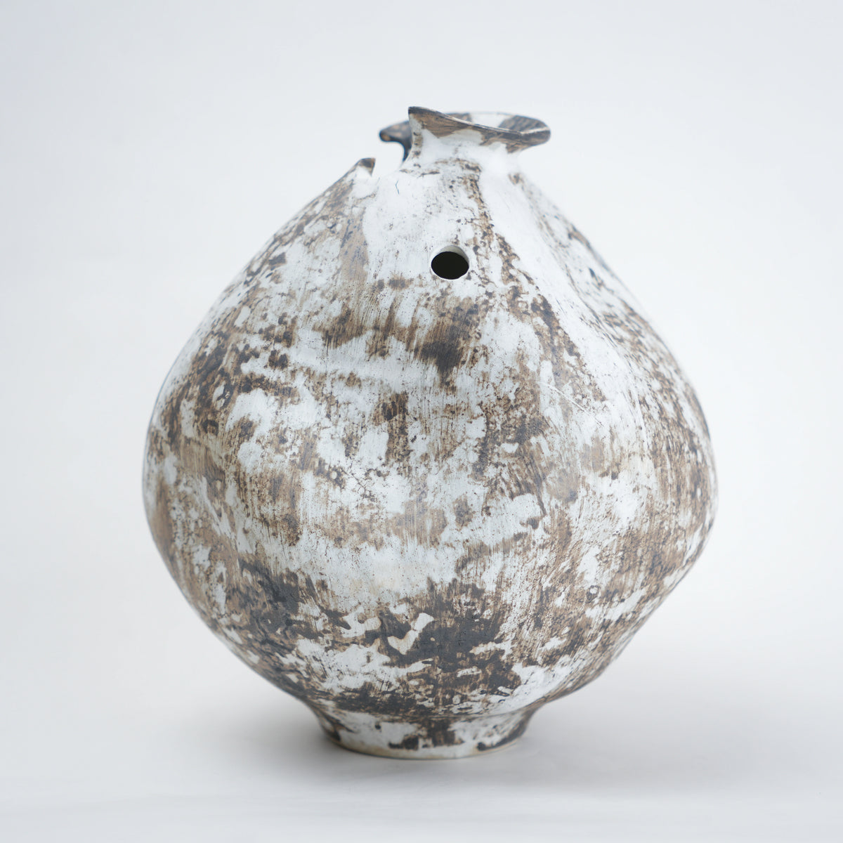 White distressed ceramic vase with rounded body and narrow base, featuring a textured rustic finish, dual side openings, and an uneven top rim, ideal for modern home decor and artistic styling.