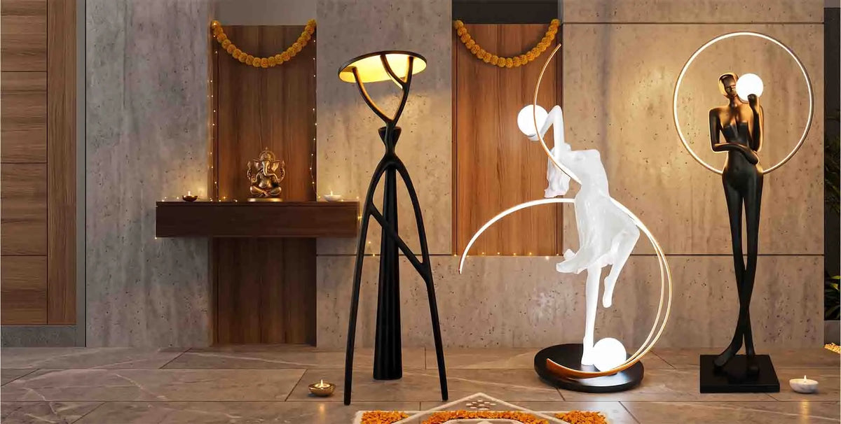 A modern home decor display featuring three distinct lamps and sculptures: a black three-legged floor lamp with a glowing bowl, a white abstract dancer sculpture with circular light rings, and a black female figurine inside a glowing ring.