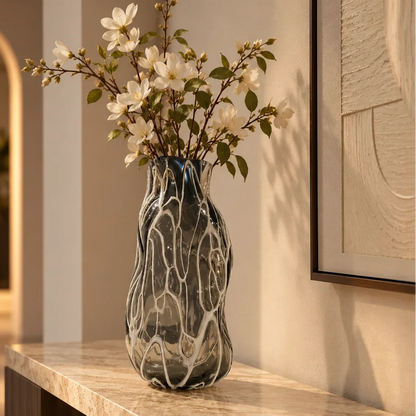 Luxury smoked glass flower vase featuring an elegant organic ripple texture and translucent grey finish, styled with vibrant floral stems for console tables, dining spaces and modern designer interiors.