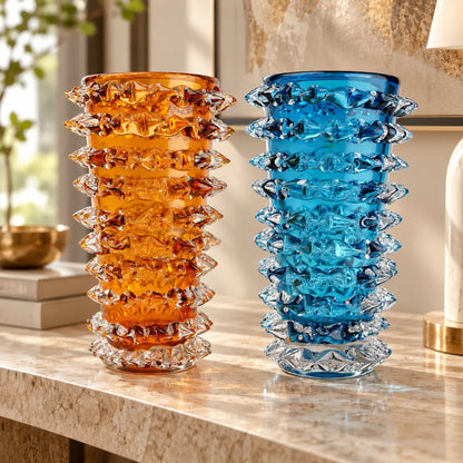 Two textured glass vases with a stacked, ruffled design, one amber orange and one bright blue, displayed on a marble console table