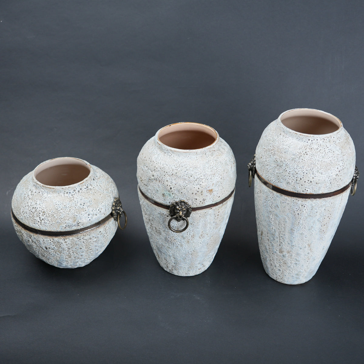 Three ceramic vases with textured surfaces and metal bands on a dark background