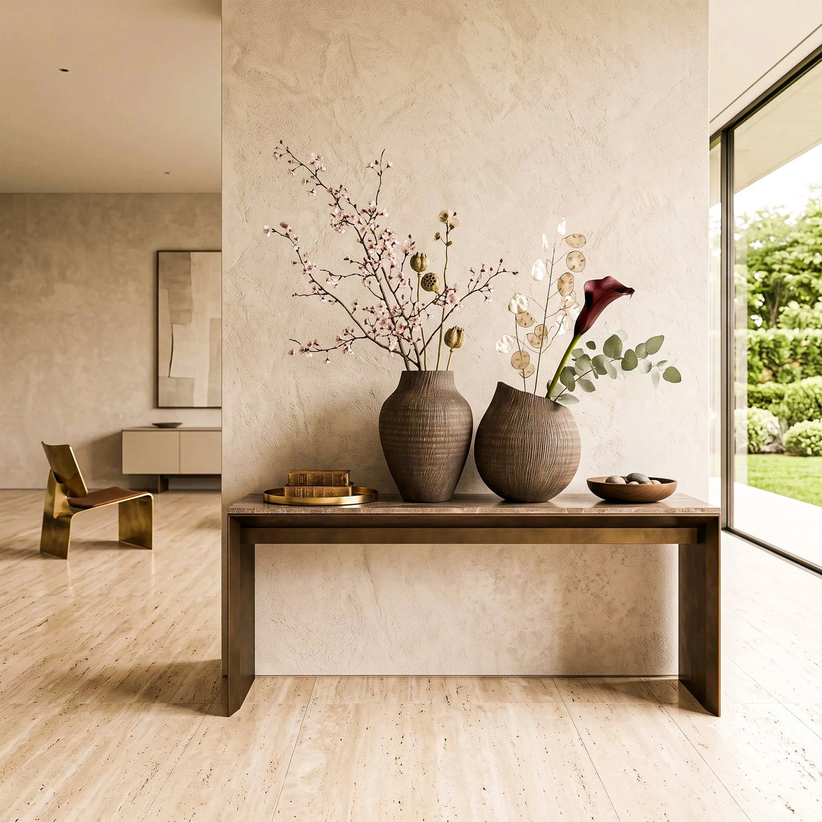 Two textured brown ceramic vases filled with dried botanicals and a red calla lily, displayed on a wooden console table in a modern, warm-toned interior with a stone wall and large windows.