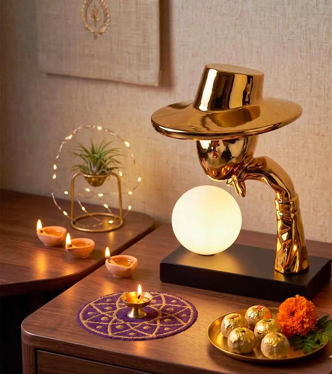 A decorative table lamp shaped like a gold-toned human figure wearing a hat, with a glowing white spherical light on a black base.