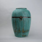 Turquoise ceramic urn with decorative elements on a light gray background