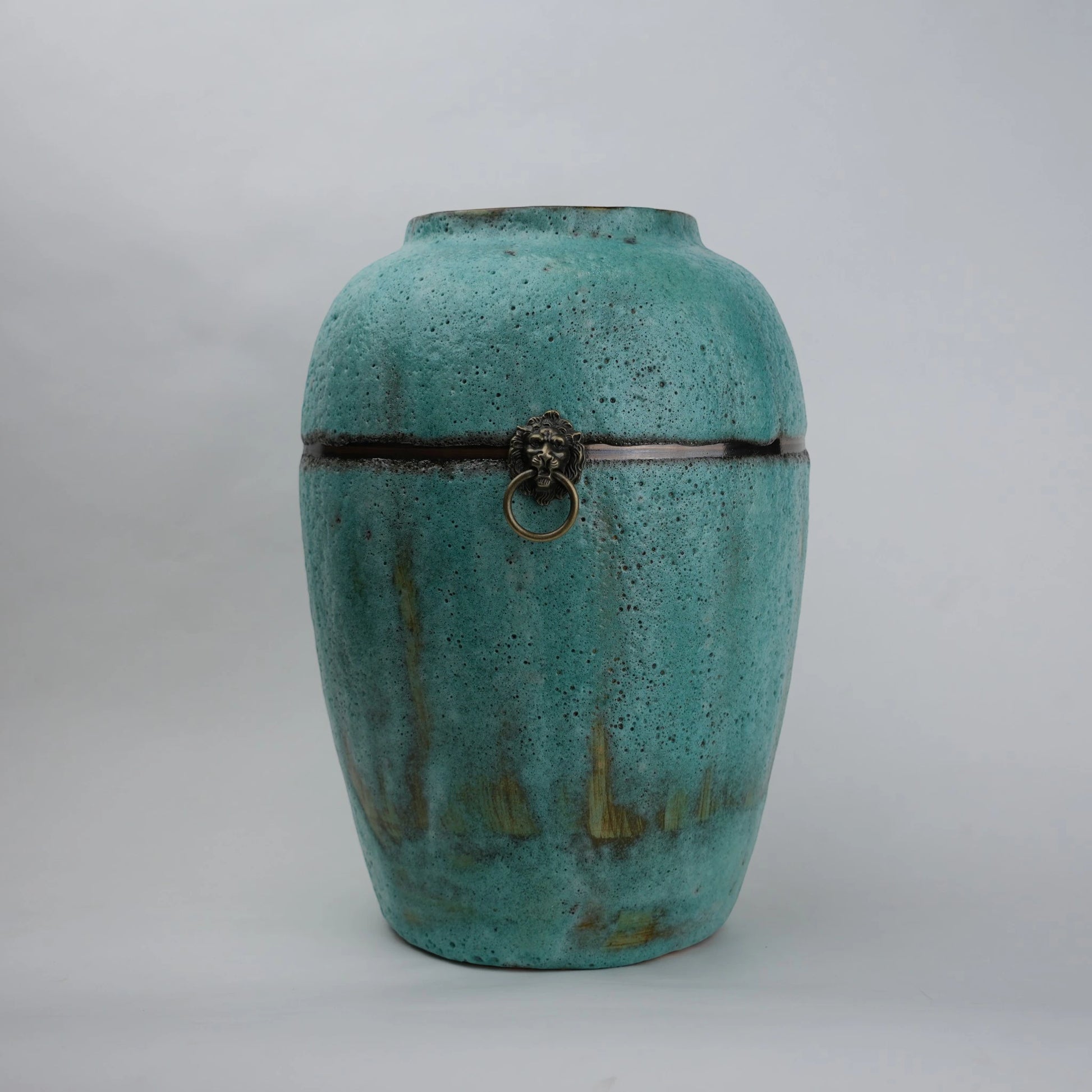 Turquoise ceramic urn with decorative elements on a light gray background