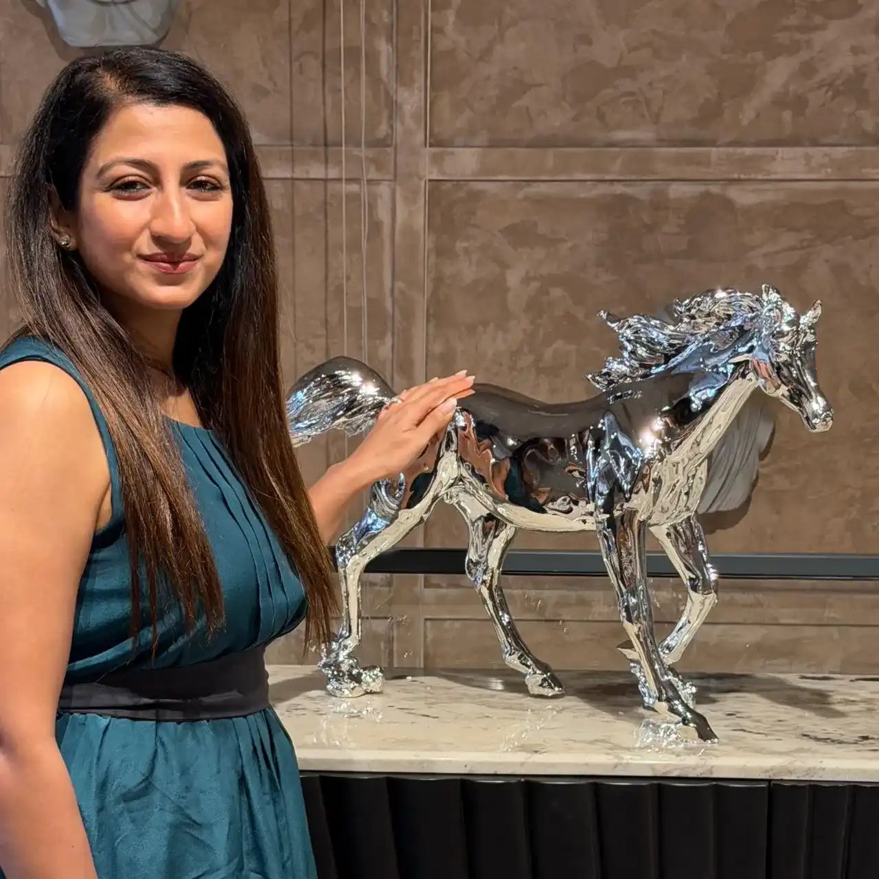 Woman standing next to a silver horse sculpture on a marble surface.