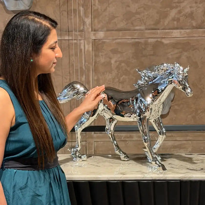 Woman interacting with a metallic horse sculpture on a marble surface.