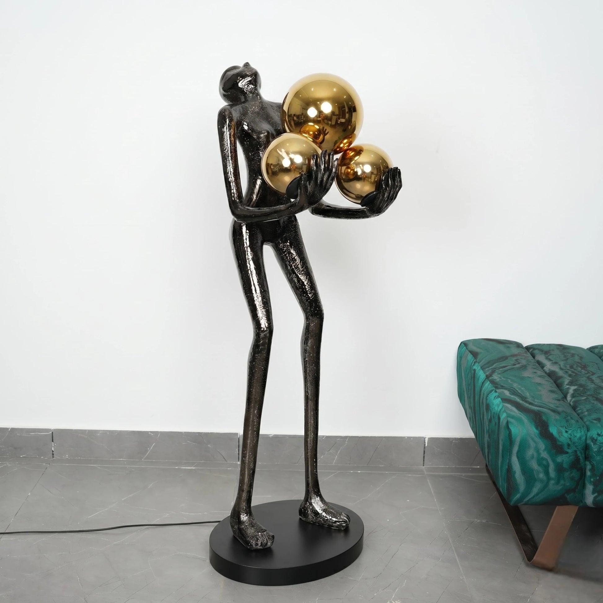 Abstract sculpture of a figure holding gold spheres on a plain background