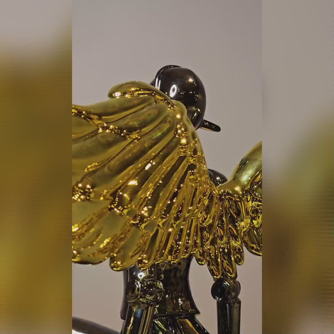 Chrome angel figurine with gold wings seated in a modern pose.