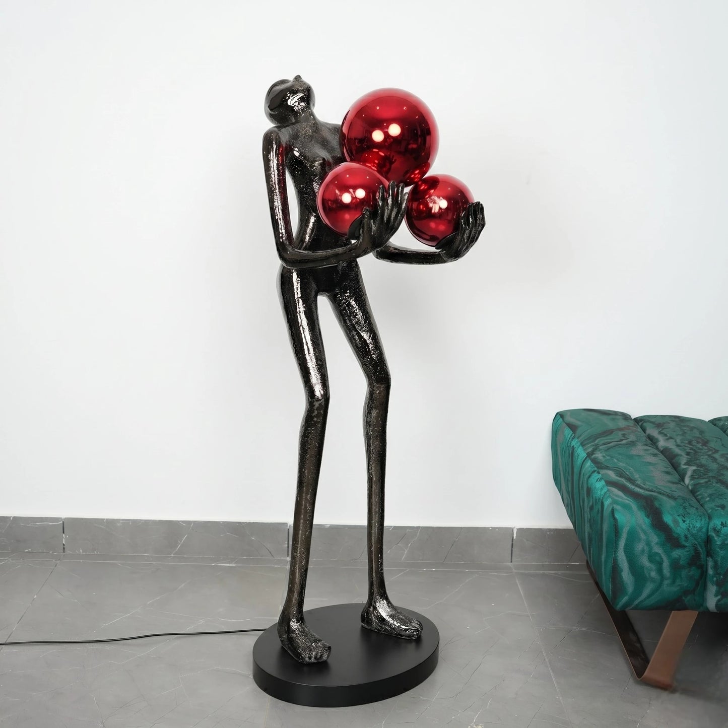 Statue of a figure holding three red spheres in a room with a green chair.