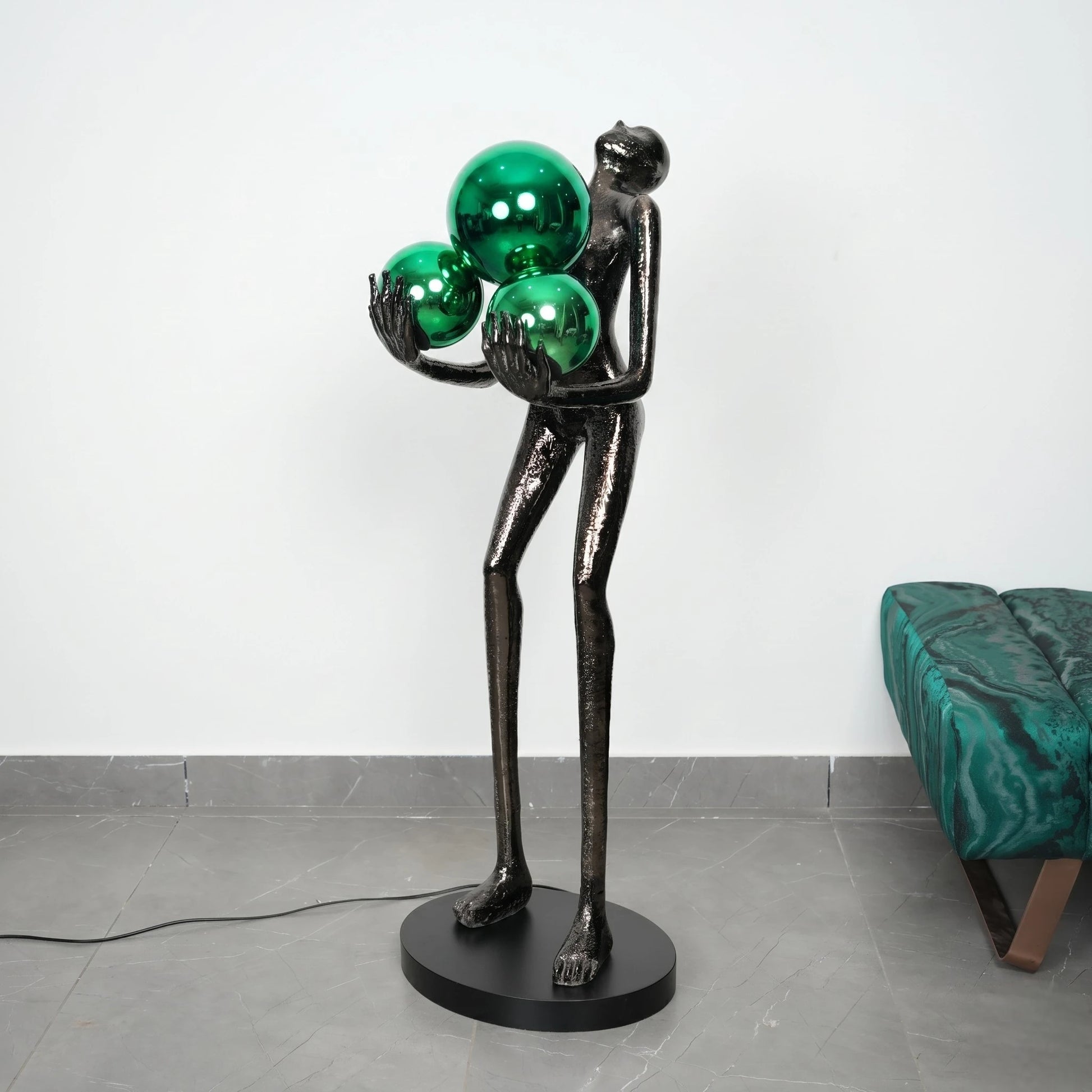Black sculpture holding three green spheres on a gray floor with a white wall background
