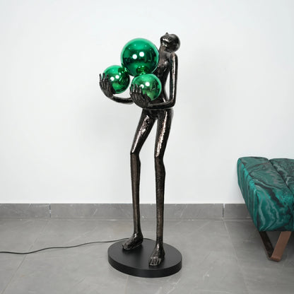 Black sculpture holding three green spheres on a gray floor with a white wall background
