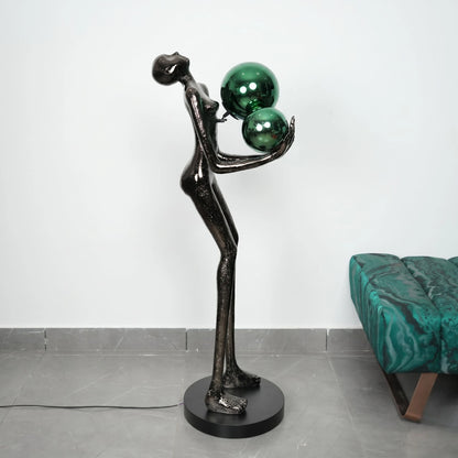 Statue of a figure balancing two green spheres on a white background