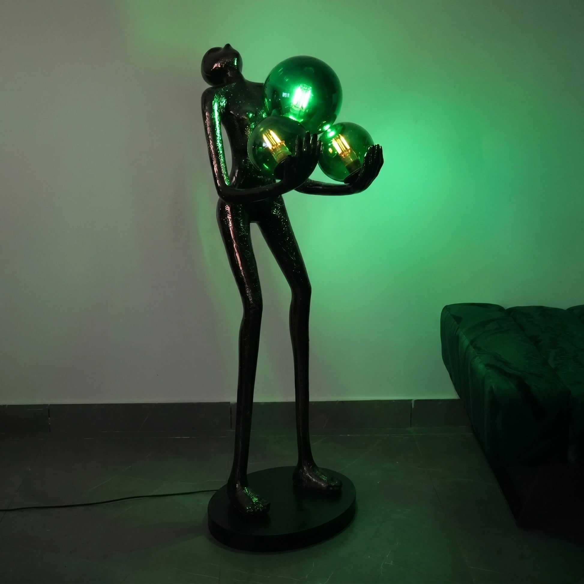 Decorative lamp with a black base and green spherical lights against a plain wall.