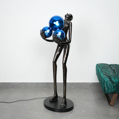 Black sculpture holding blue spheres on a gray floor with a white wall background